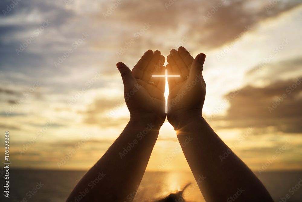 A person is holding a cross in their hands at sunset