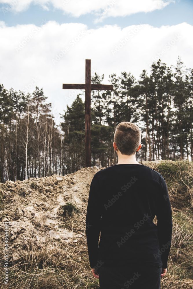 A man is standing in front of a wooden cross in the woods.