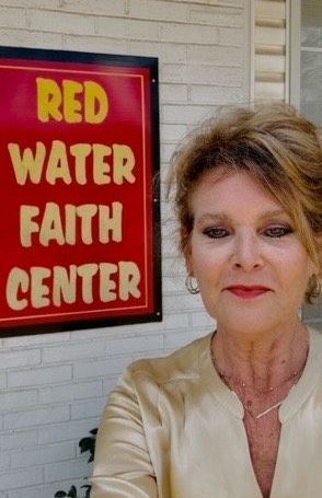 A woman is standing in front of a red water faith center sign.