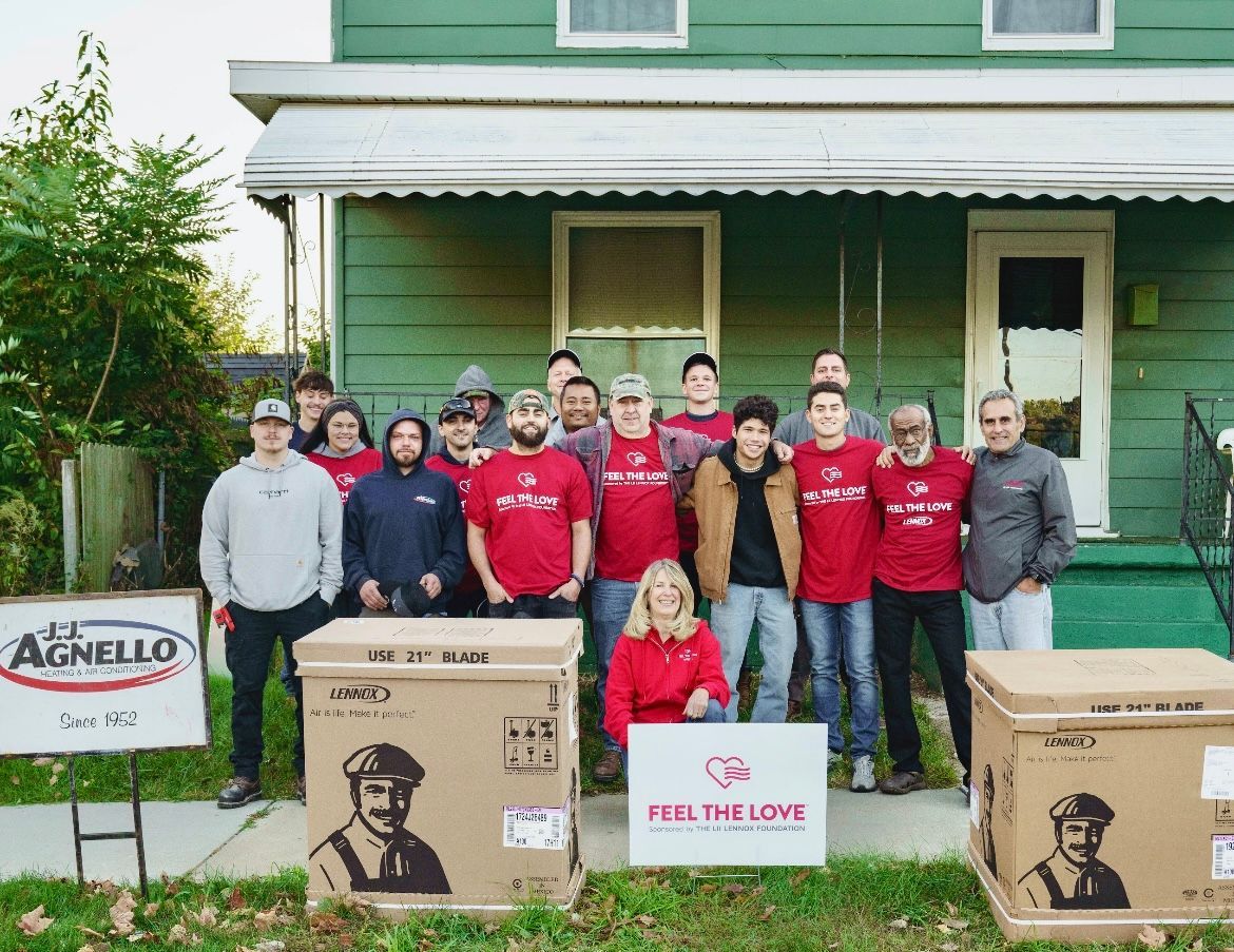 A group stands in front of a green house with two boxes marked