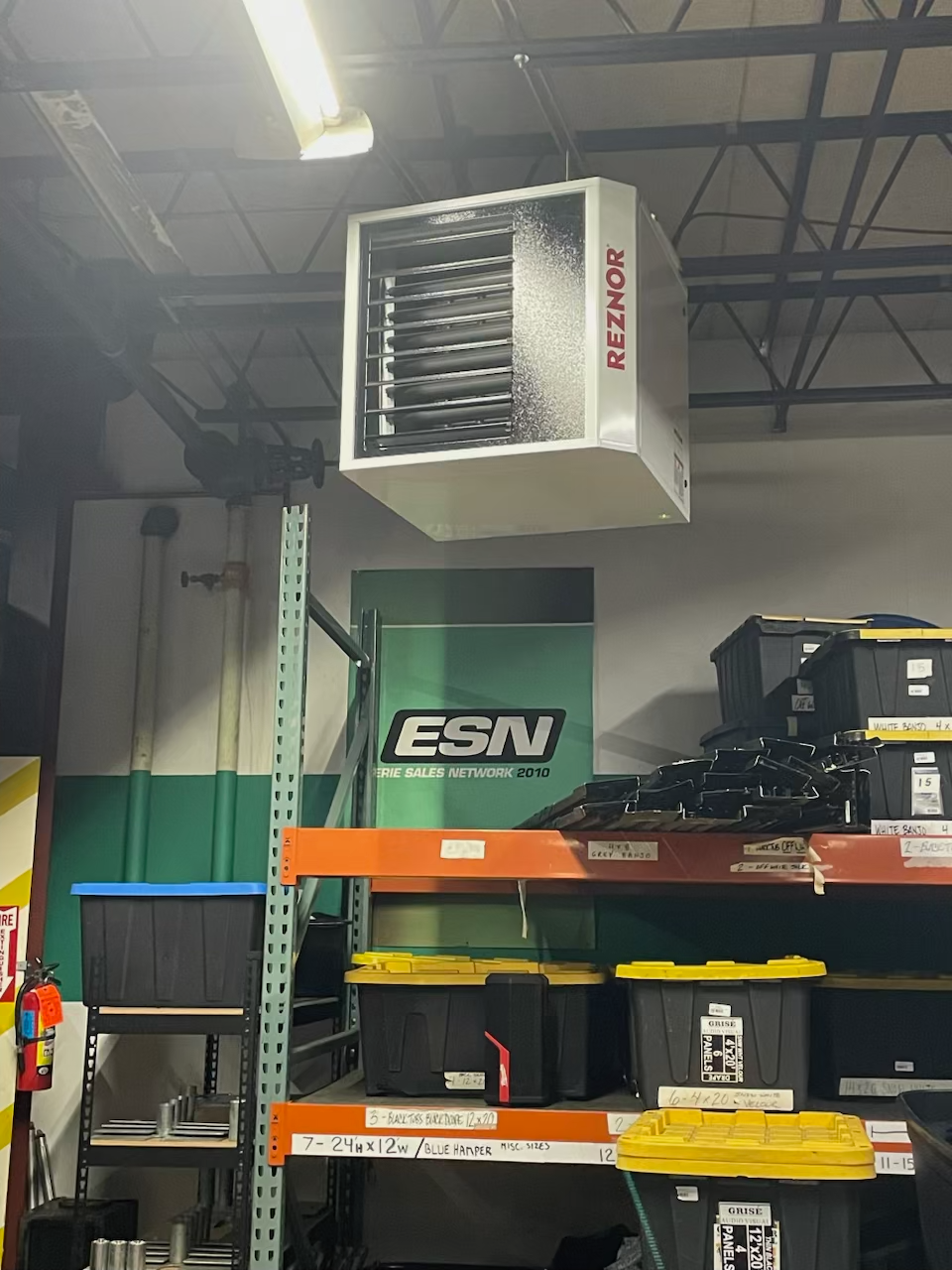 A Reznor unit heater suspended from the ceiling above warehouse shelving units stocked with storage bins.