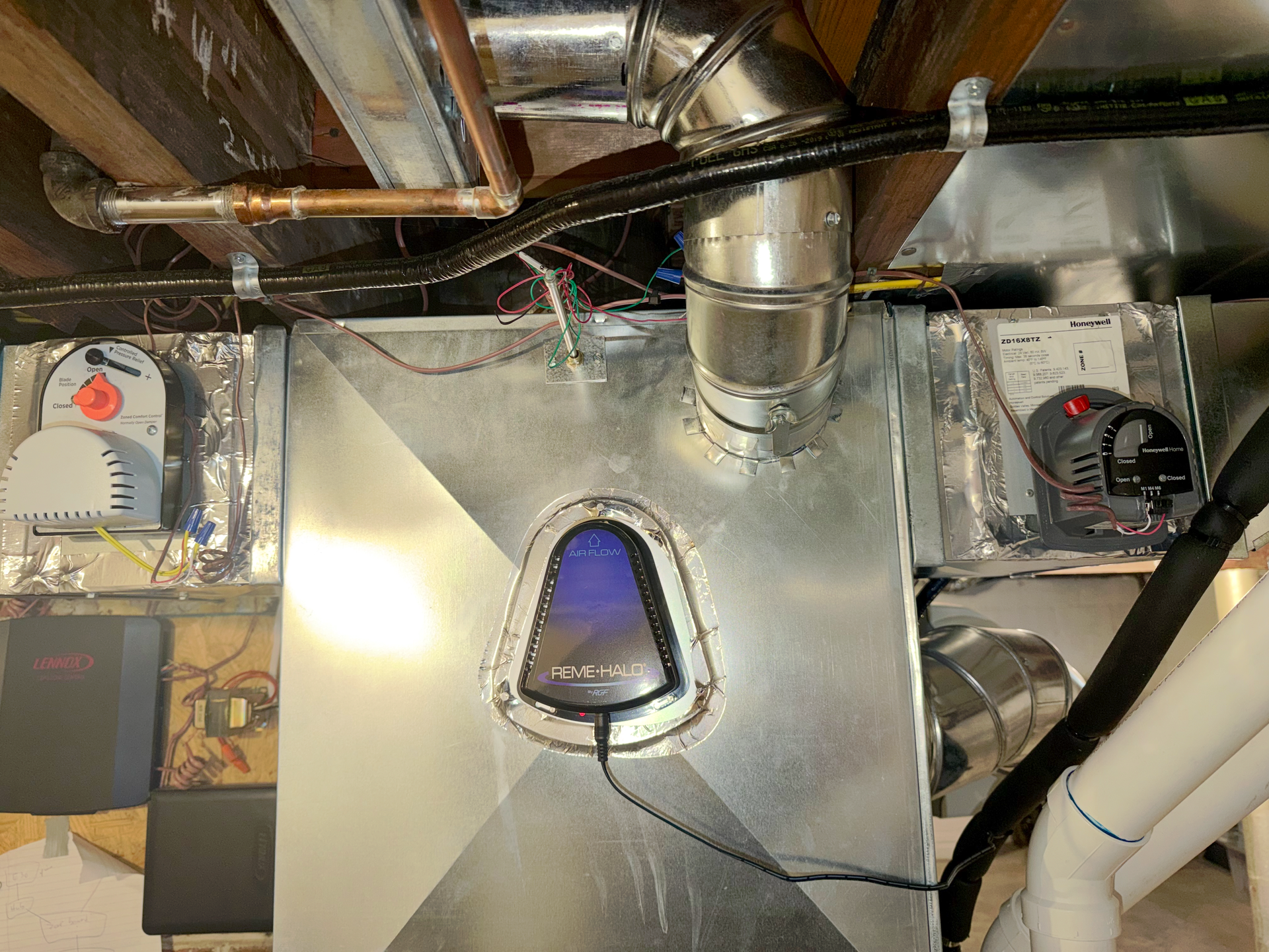 An HVAC air purification system installed on metal ductwork with various electrical components and piping in a basement.