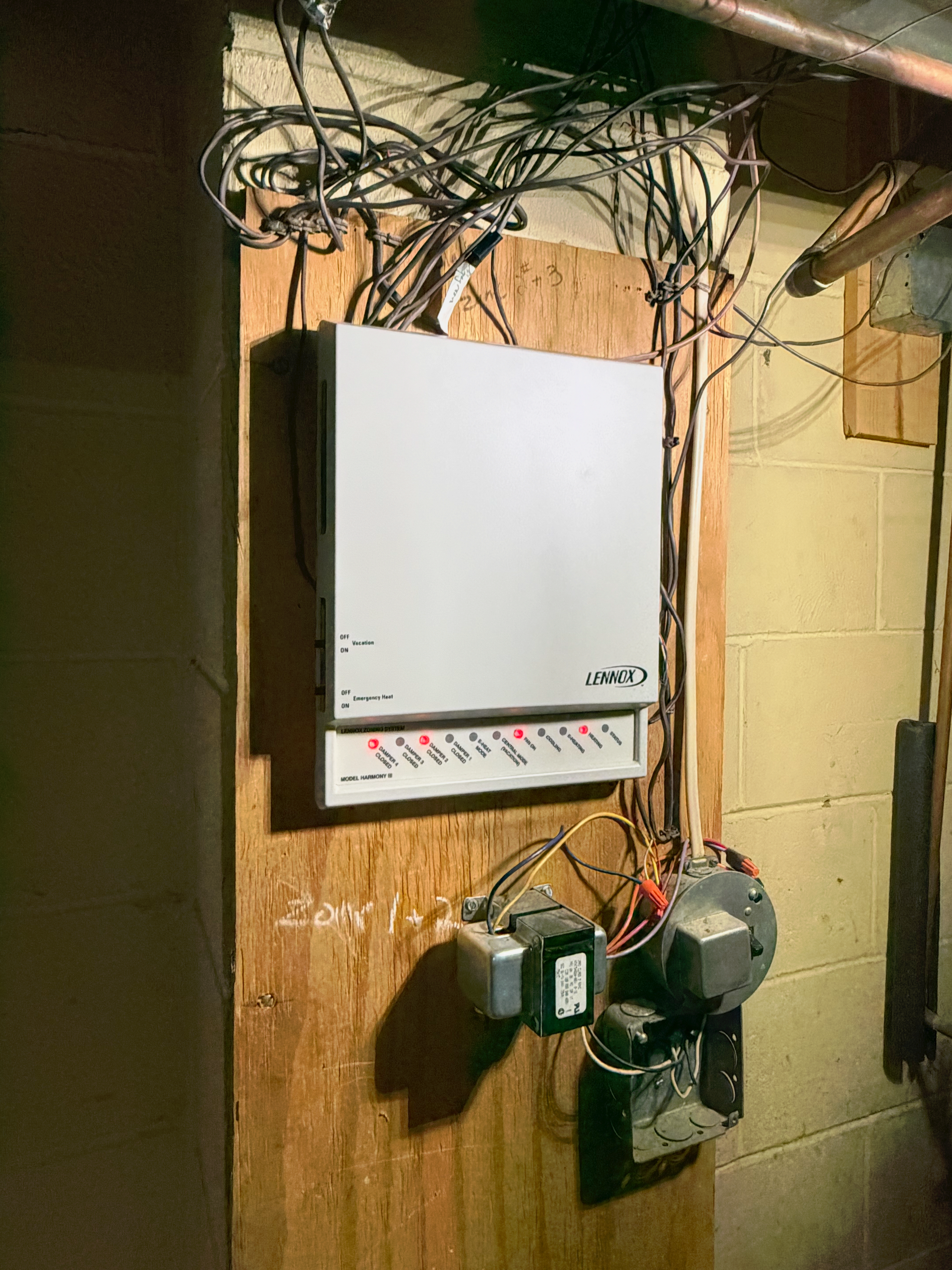 A white alarm system control box with illuminated red status lights mounted on a wooden board with exposed wiring.