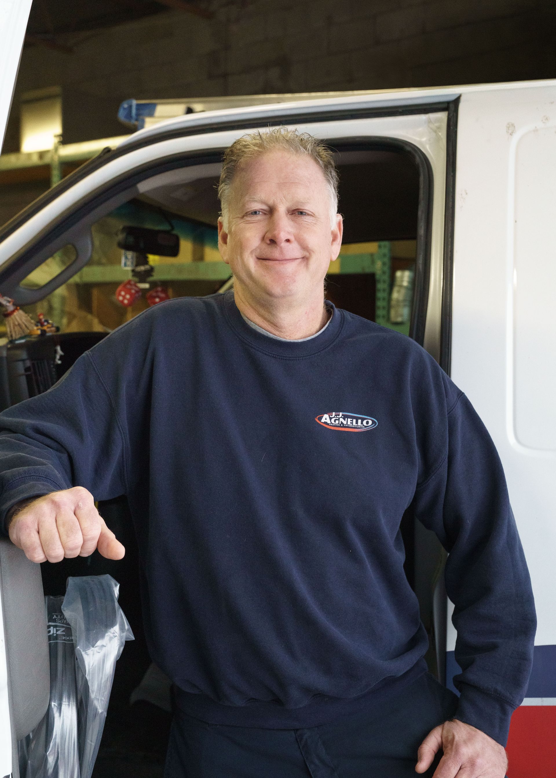 A person in a dark blue sweater smiling while standing in the doorway of a work van.
