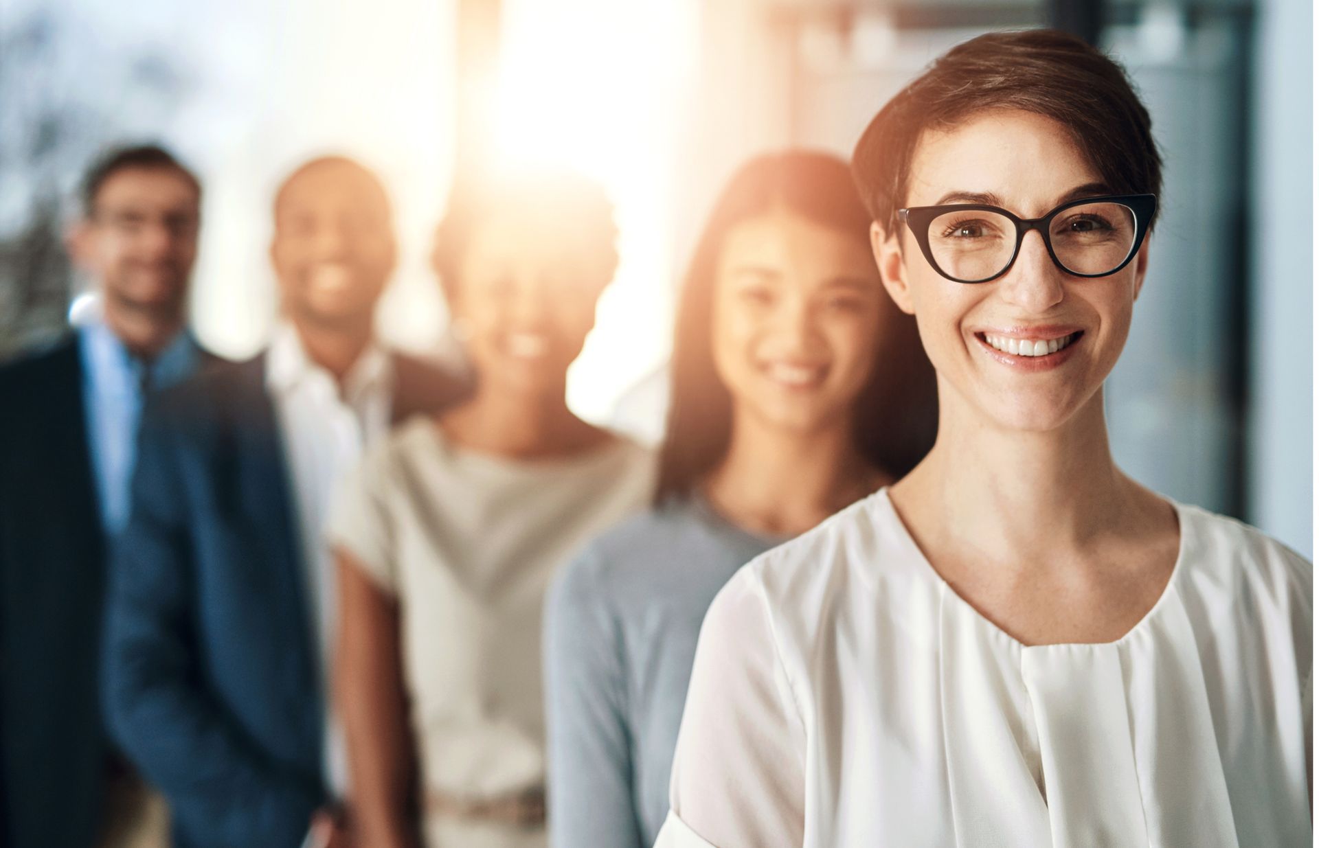 A woman wearing glasses is standing in front of a group of people.
