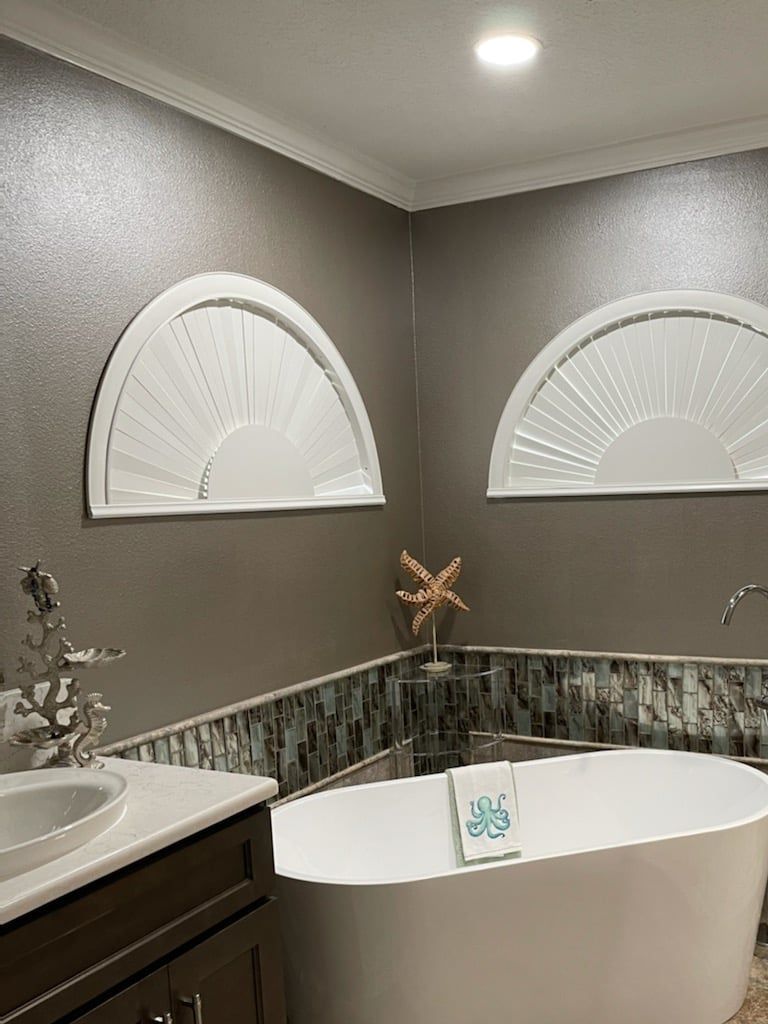 Modern bathroom with freestanding tub, gray walls, and two half-circle windows above wainscoting.