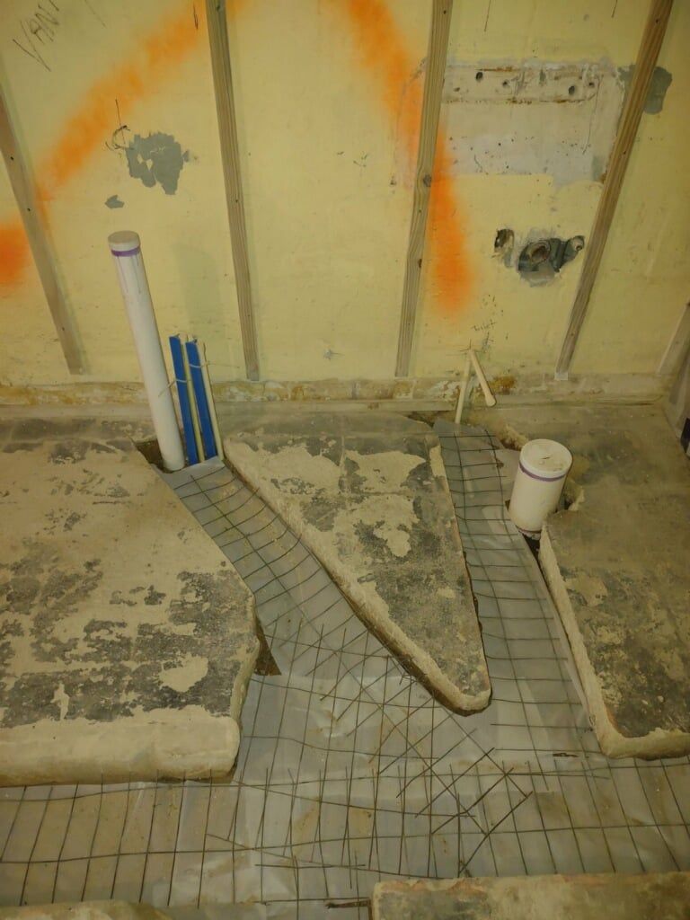 Bathroom under renovation with exposed plumbing, tiled floor, and scattered construction debris