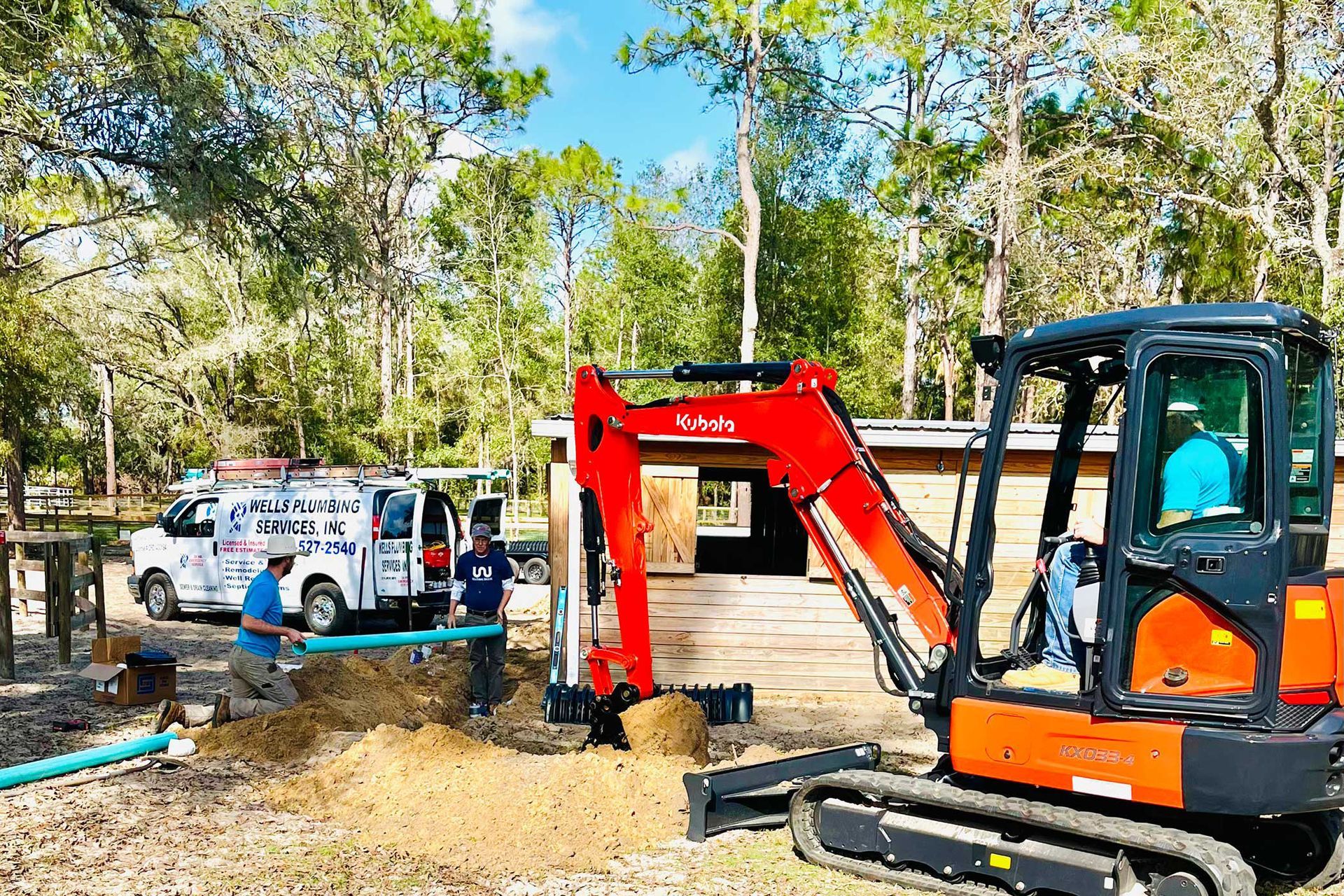 Excavator digging soil beside a utility truck in a wooded outdoor worksite
