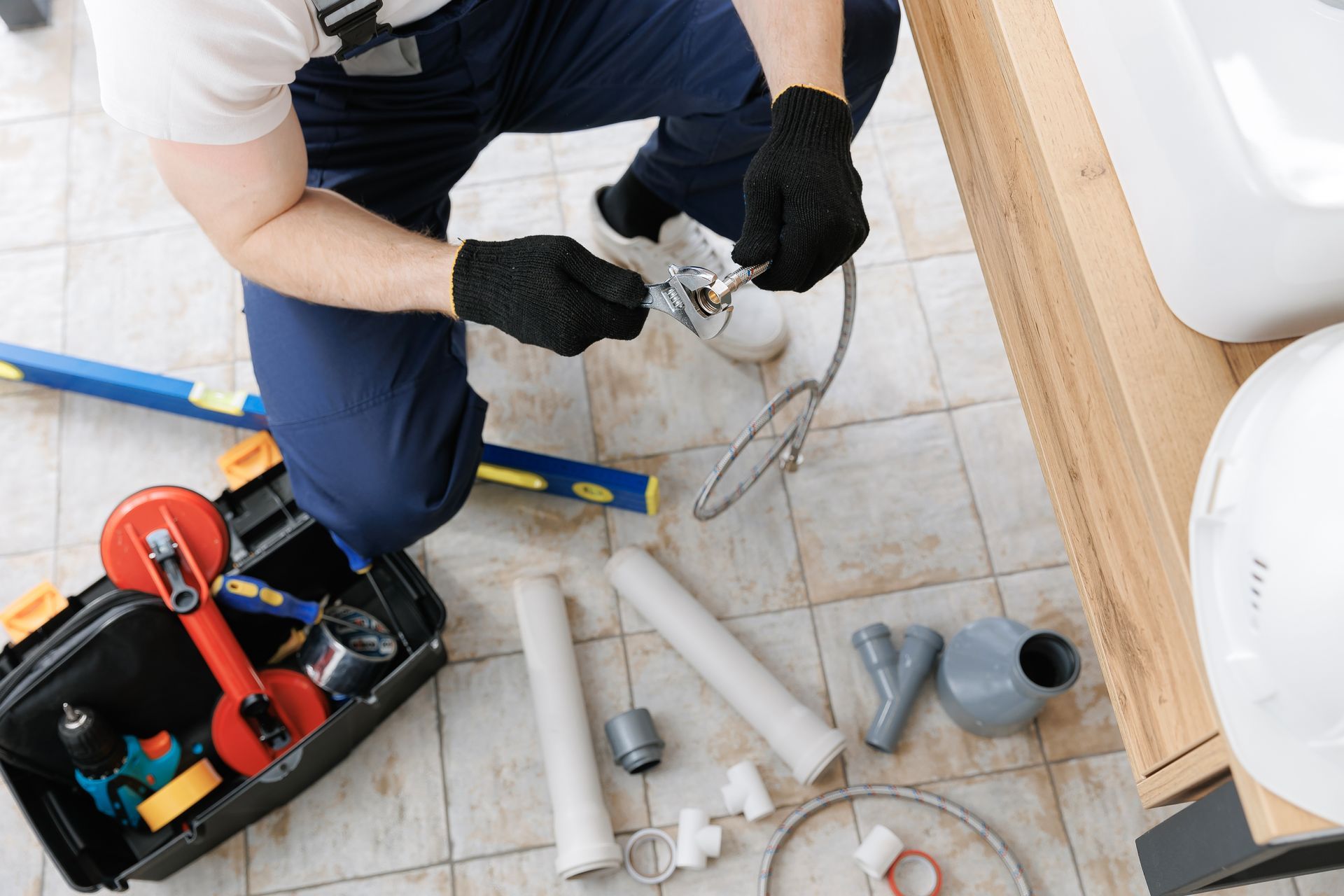 Plumber repairing a sink drain with tools on a tiled bathroom floor