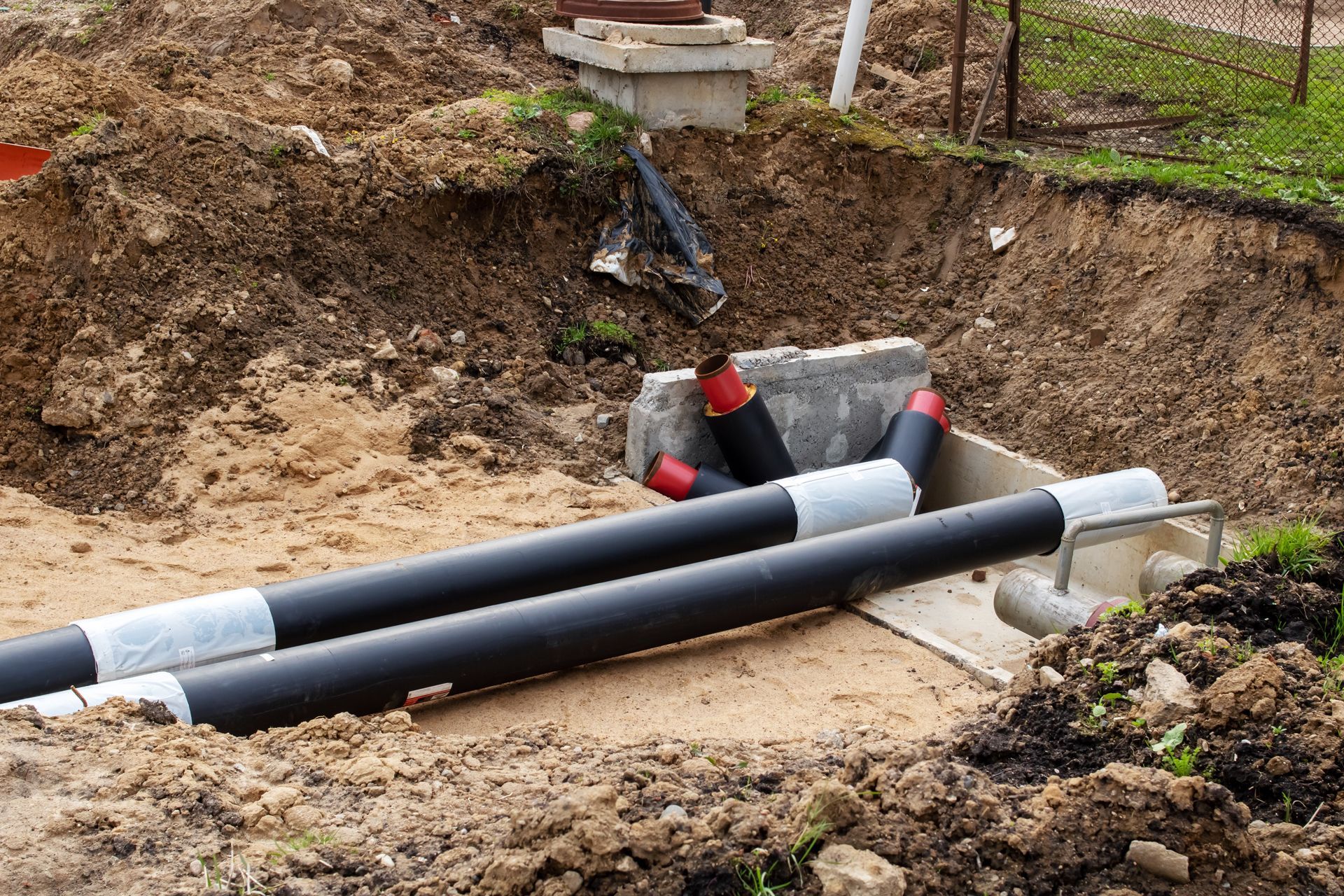 Open trench with large black and gray utility pipes being installed underground