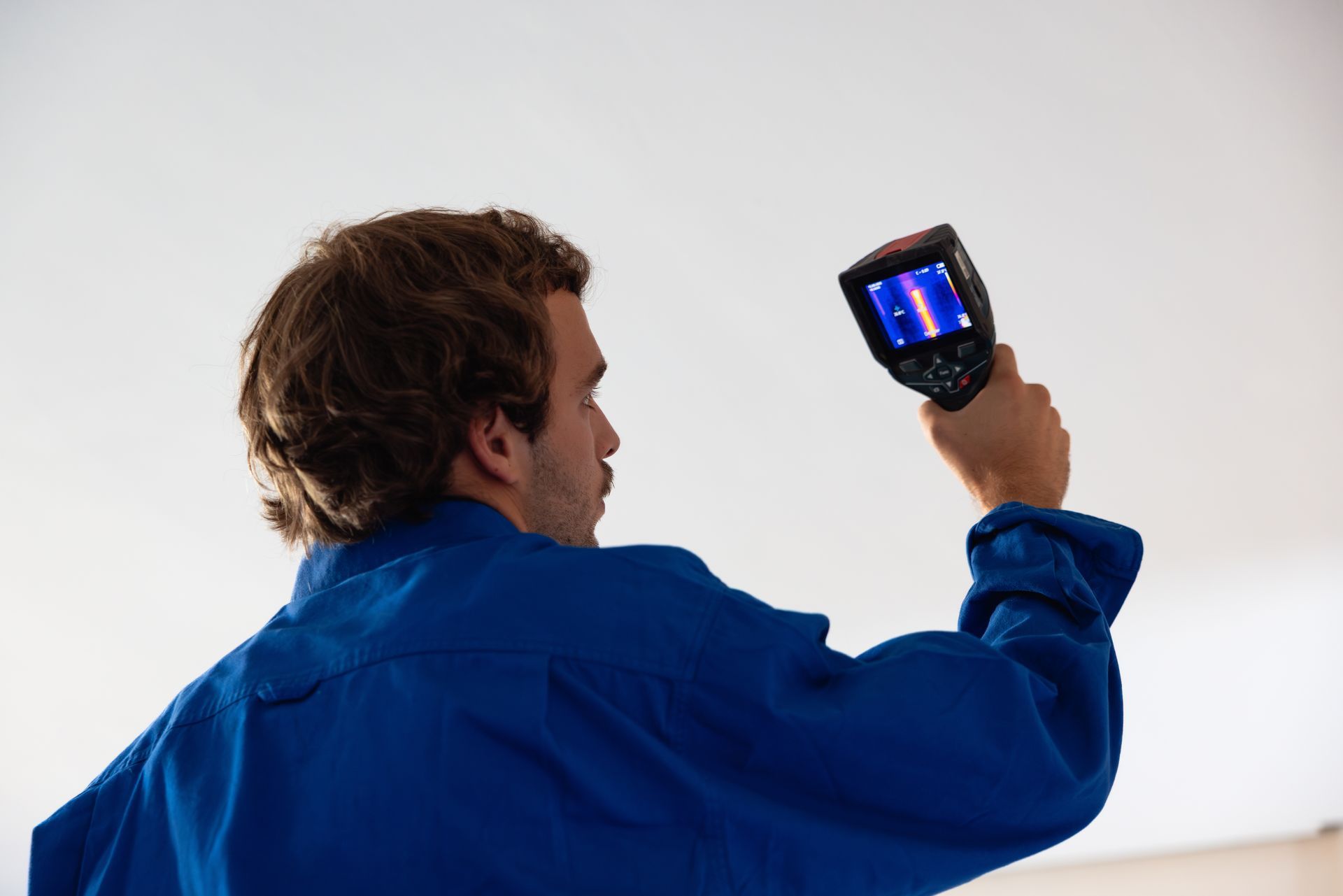 Person in blue work shirt holding a thermal camera up toward a ceiling