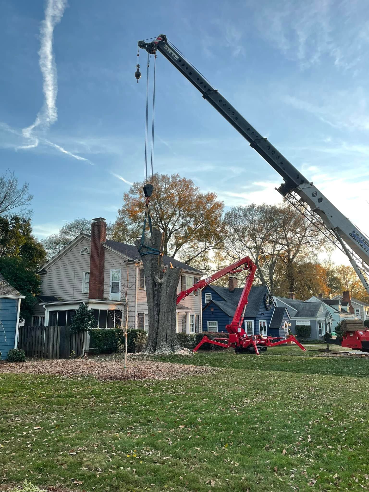 Crane lifting materials near a house with autumn trees and a blue sky
