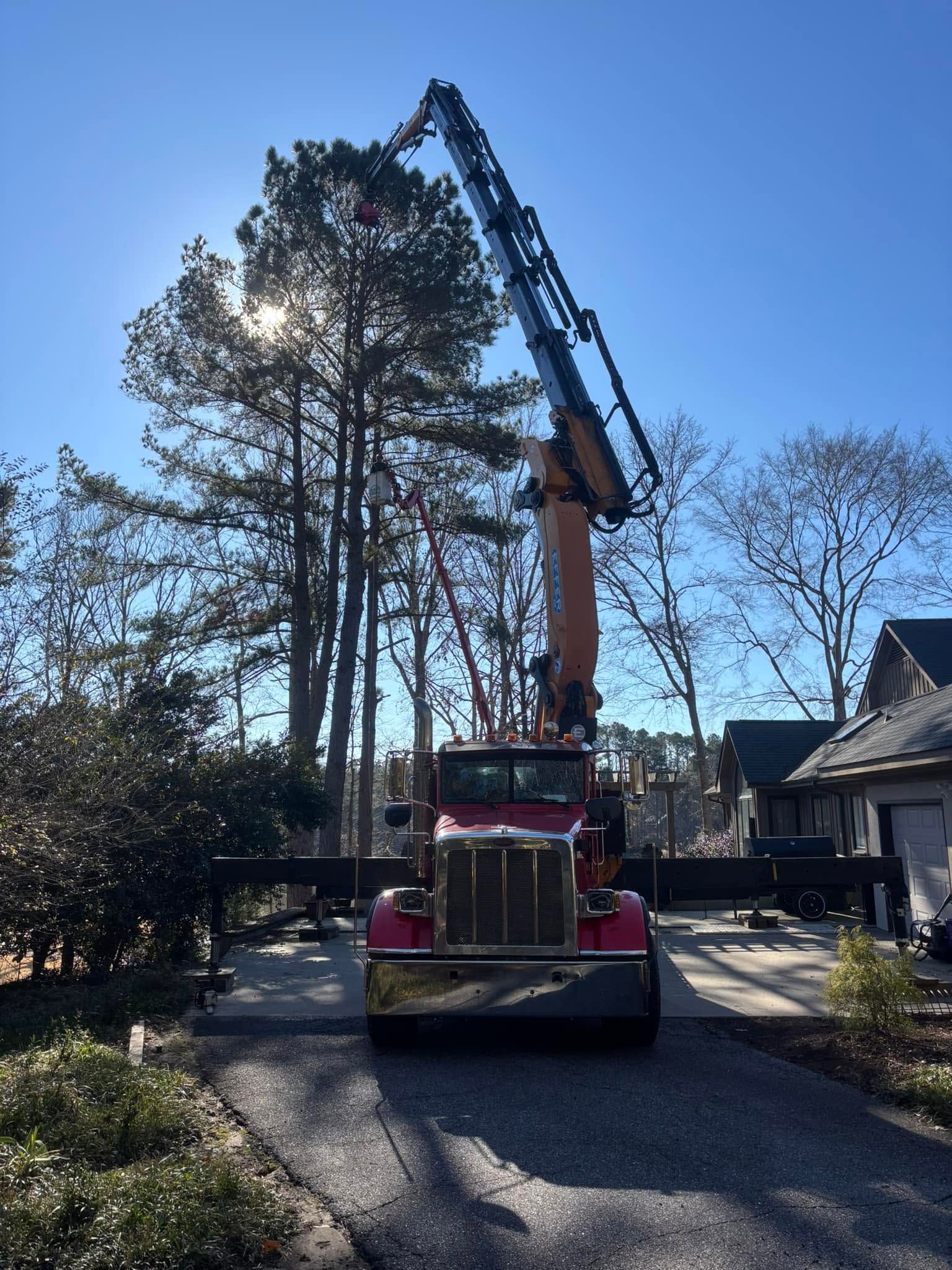 Crane truck lifting a large tree beside a house on a sunny residential street