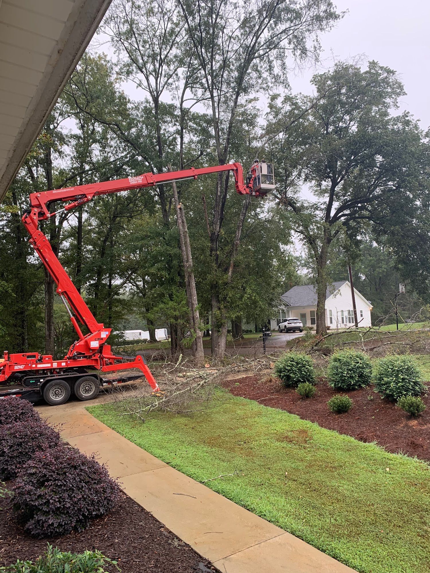Red cherry picker lifting a worker beside a house in a wooded yard