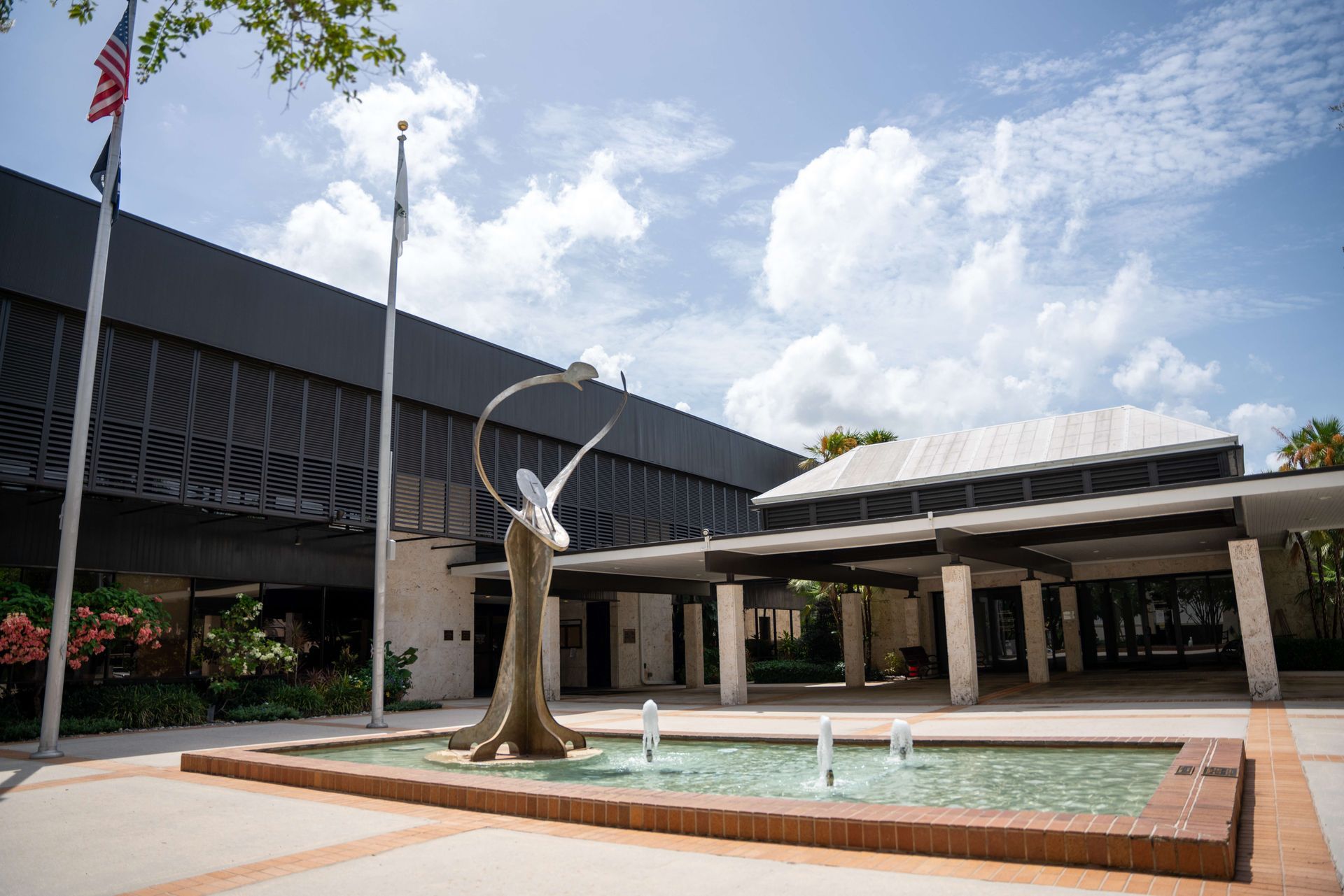 Exterior of a modern building with a fountain and sculpture under a bright sky.