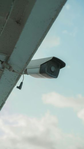 Gray security camera mounted under an overhang, angled toward the sky.