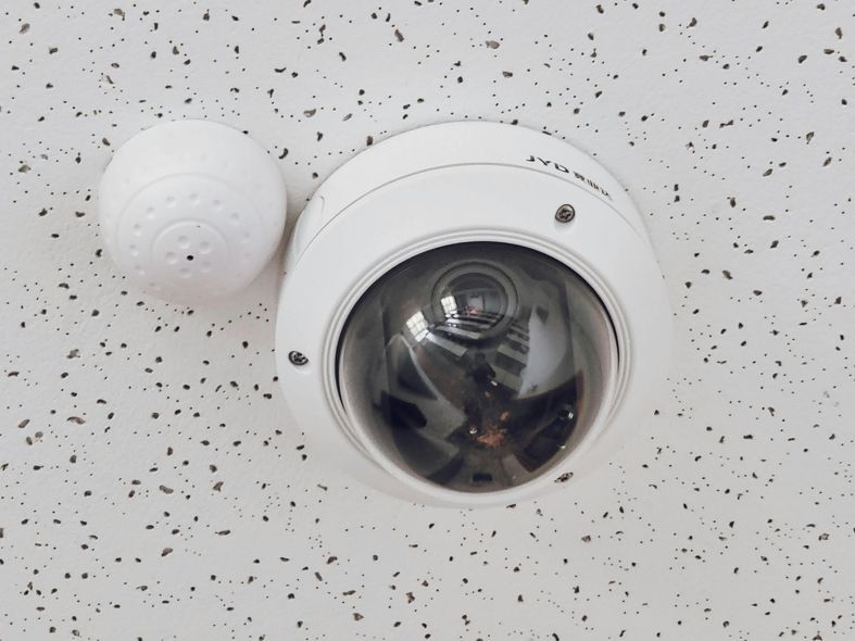 Ceiling-mounted security camera and motion sensor on a speckled white ceiling