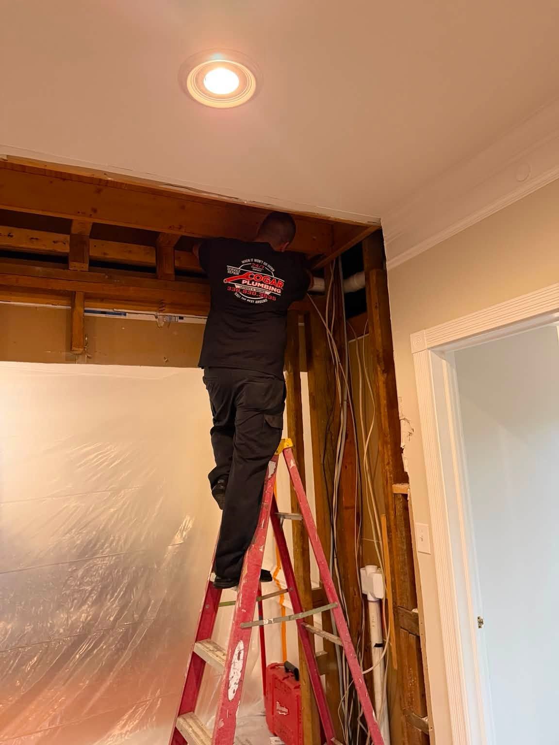 Person on a red ladder repairing ceiling in a room with plastic sheeting and exposed beams
