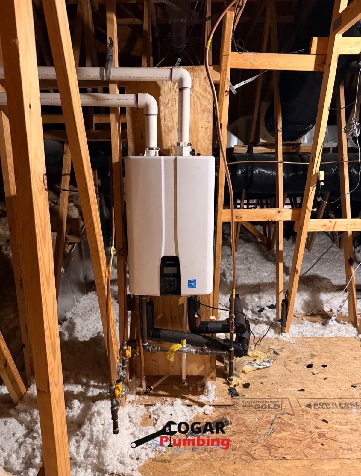 White wall-mounted boiler in an unfinished attic with exposed wooden framing and pipes.