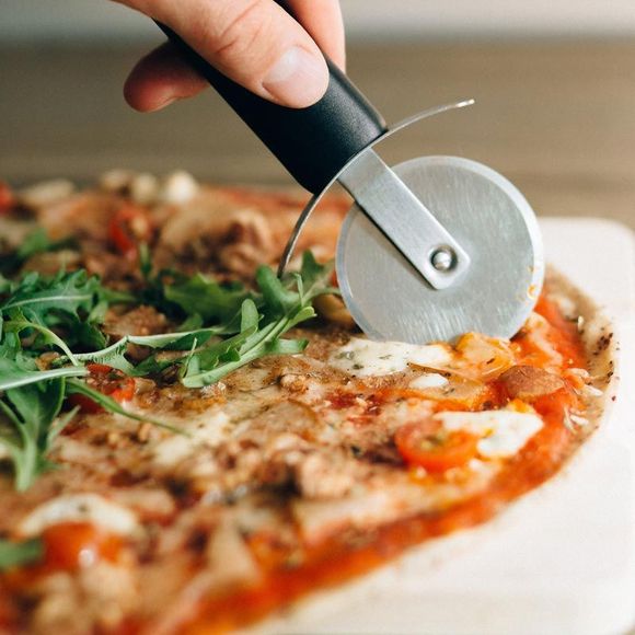 Hand slicing a pizza with a wheel cutter; arugula topping visible.