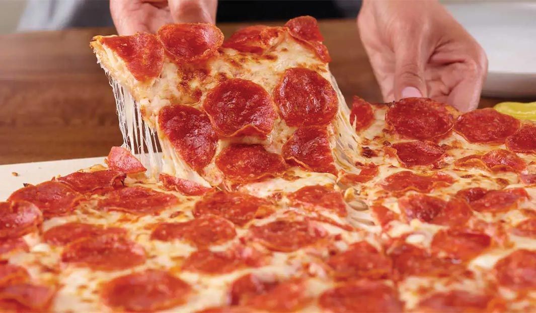 A hand pulling a slice of pepperoni pizza, cheese stretching; close-up view.