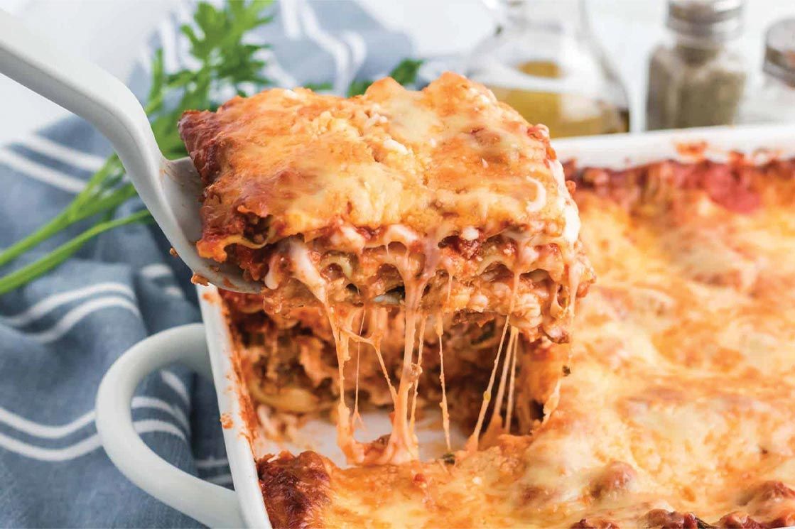 Lasagna being served from a white baking dish, cheese stretching.
