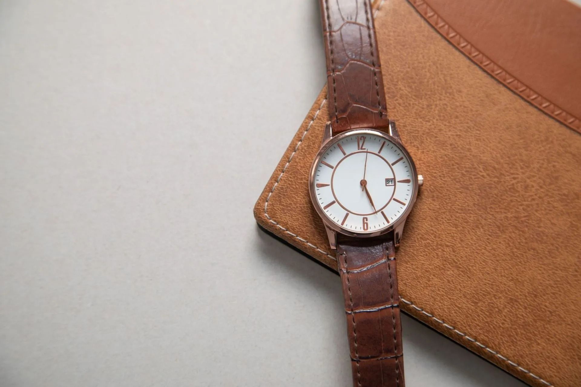 Brown Leather Watch on a Tan Leather Wallet, Set on a Light Gray Surface — Coastal Clocks & Watches in Buddina, QLD