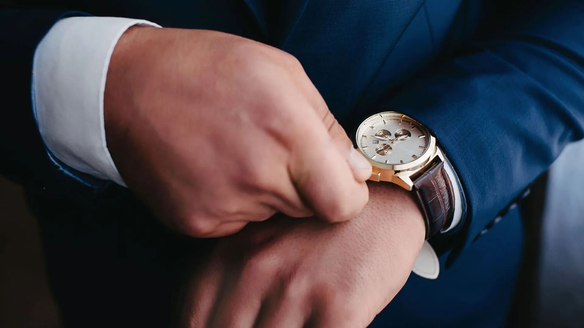 Man in Blue Suit Adjusts a Gold Wristwatch With Brown Leather Strap — Coastal Clocks & Watches in Buddina, QLD