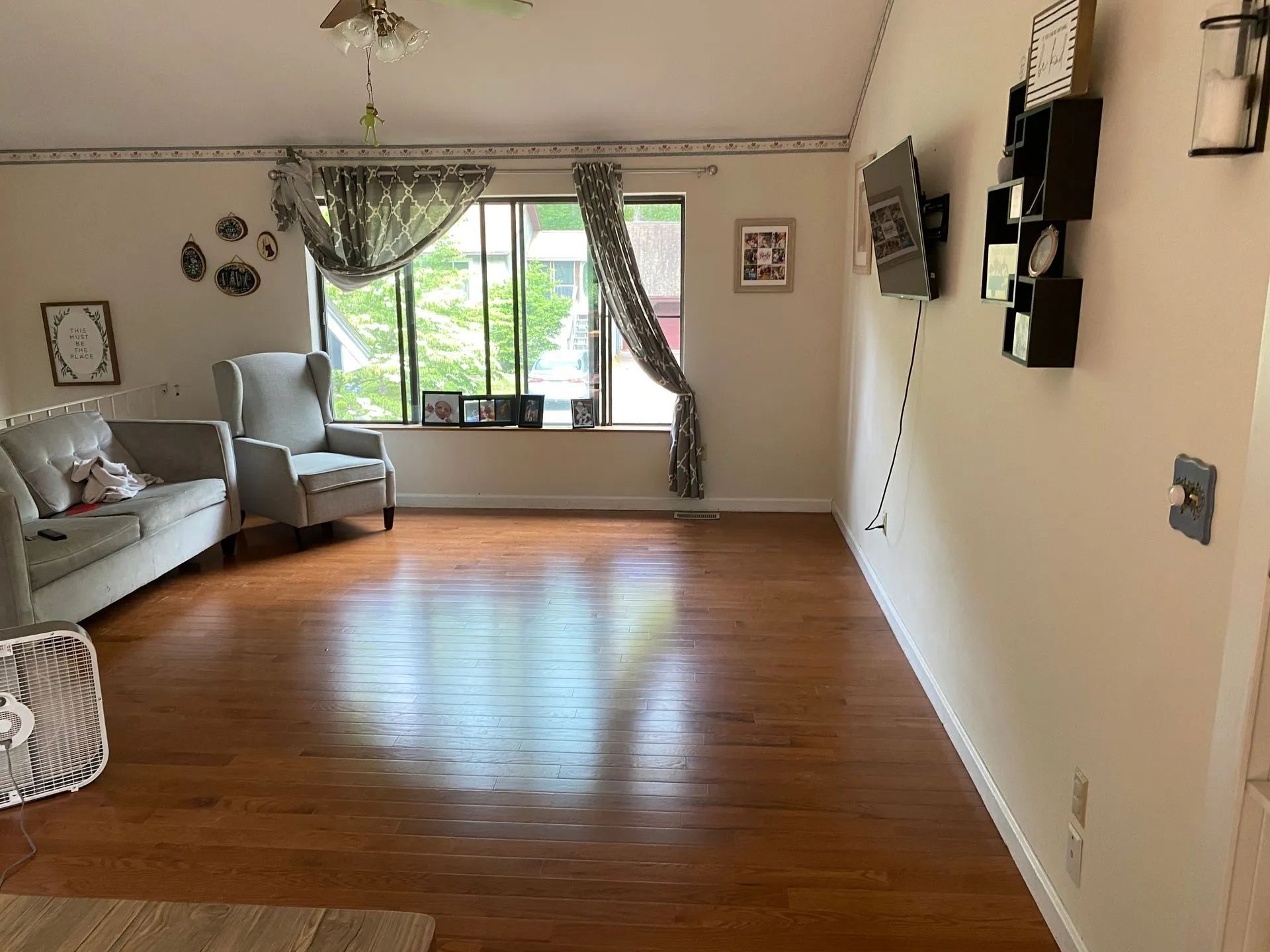 Spacious living room with hardwood floors, a window with curtains, and a couch, chair and fan.
