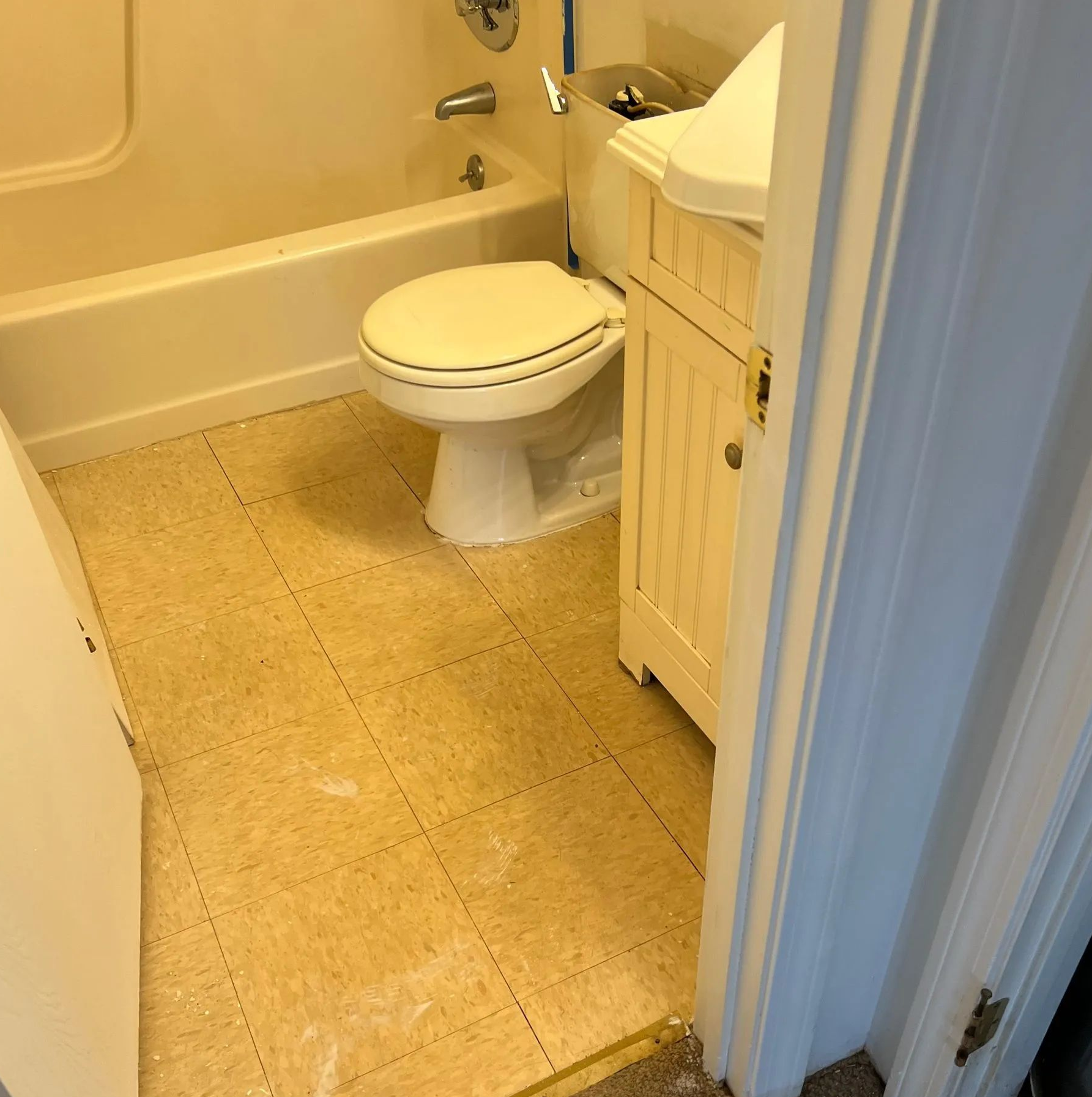 Small bathroom with a toilet, bathtub, and sink vanity on beige tile floor.