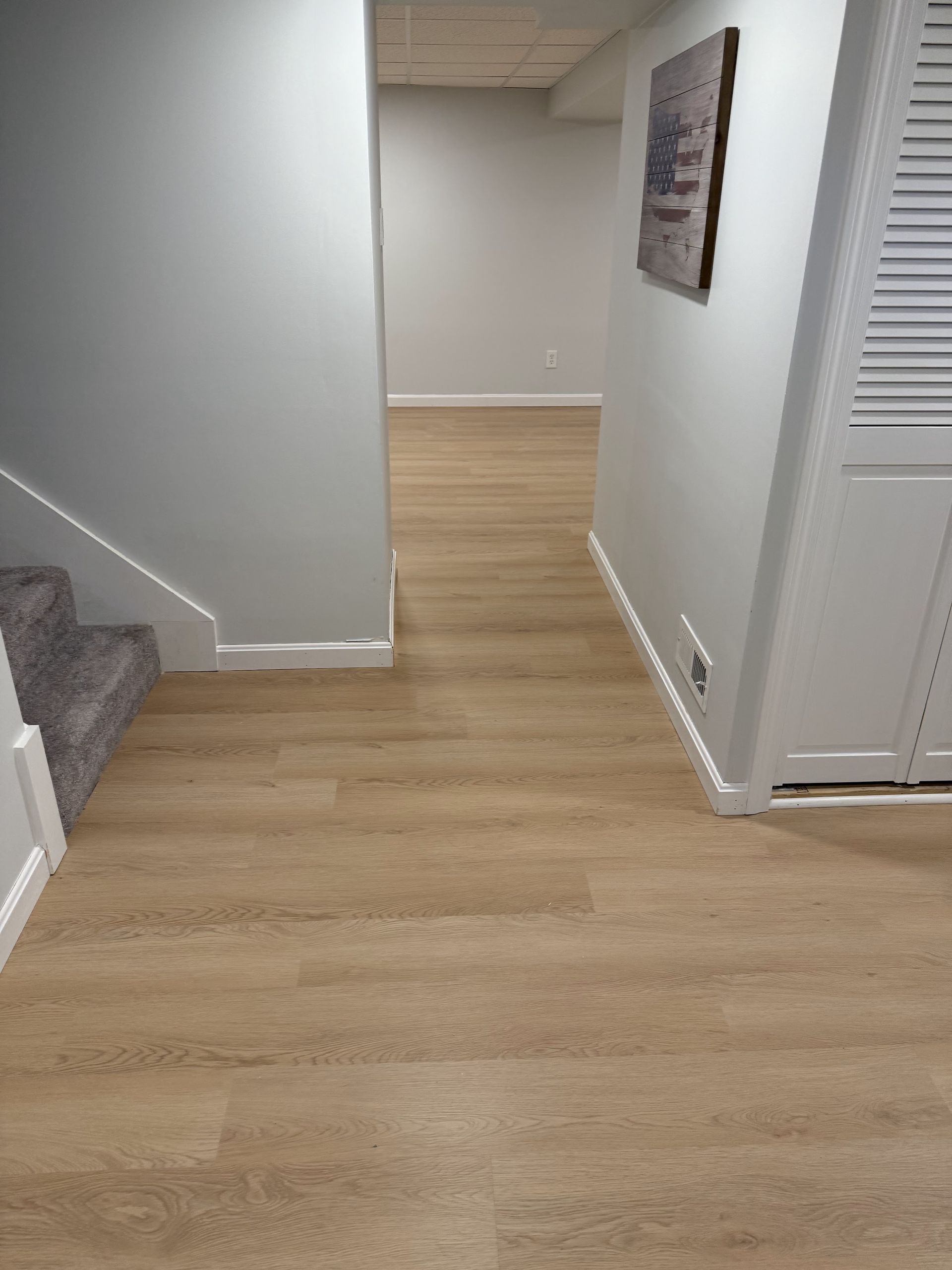 A hallway with hardwood floors and stairs in a basement.