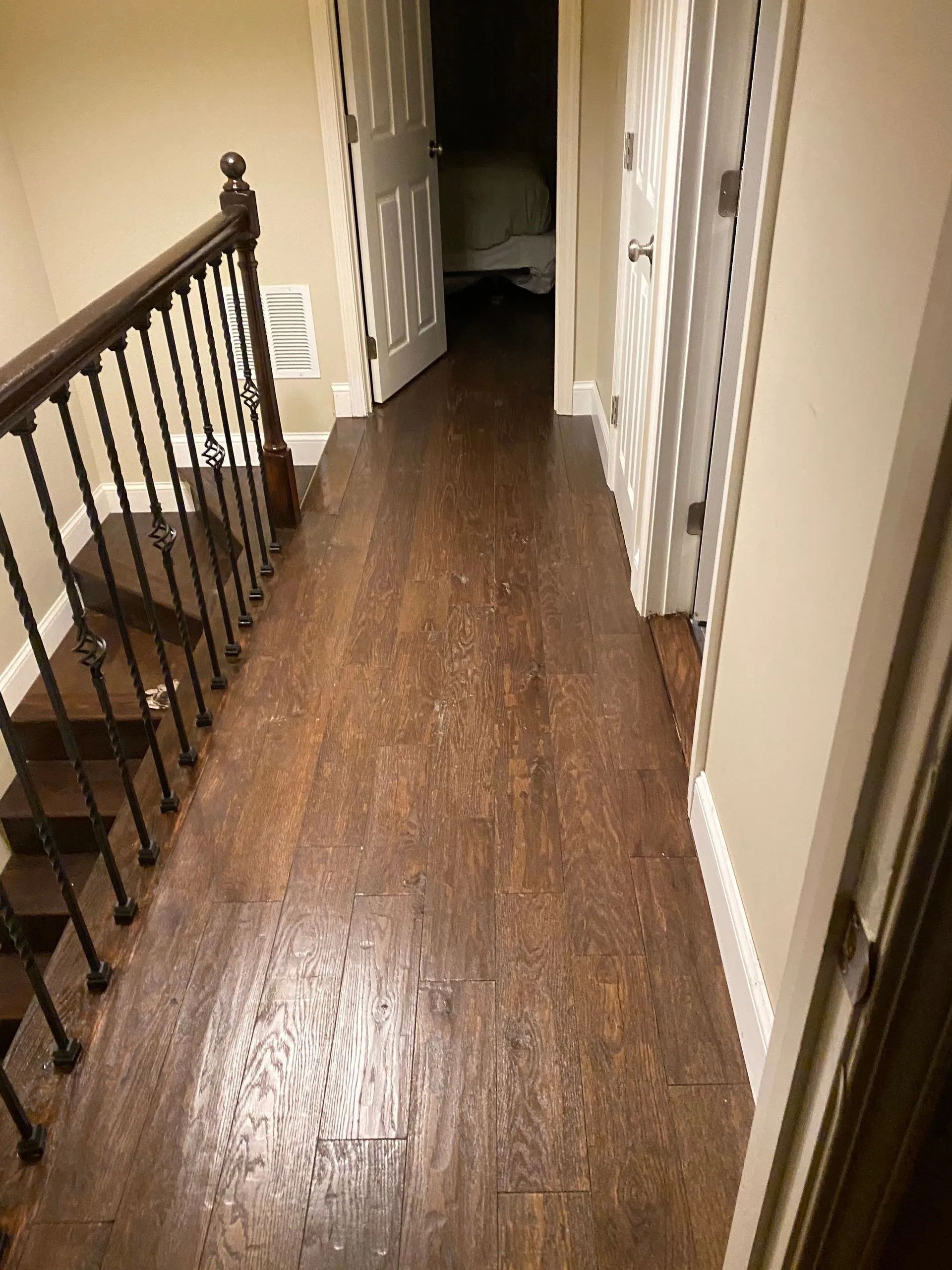 Narrow hallway with dark wood floor, beige walls, black railing, and doors on both sides.