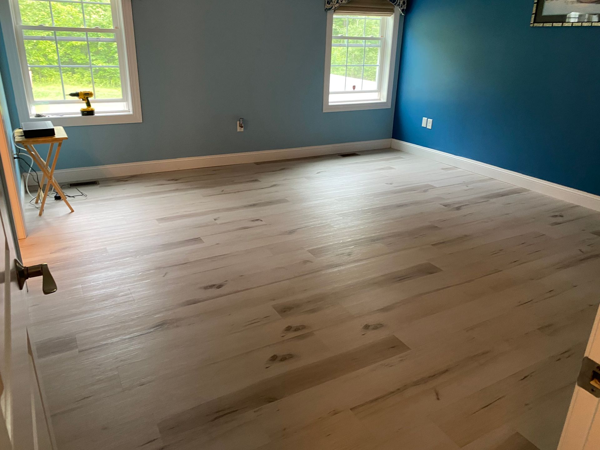 A bedroom with blue walls and white hardwood floors.