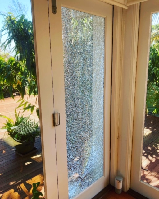 White-framed door with shattered glass; a sunny outdoor setting visible through it — Long Jetty Glass in The Entrance, NSW