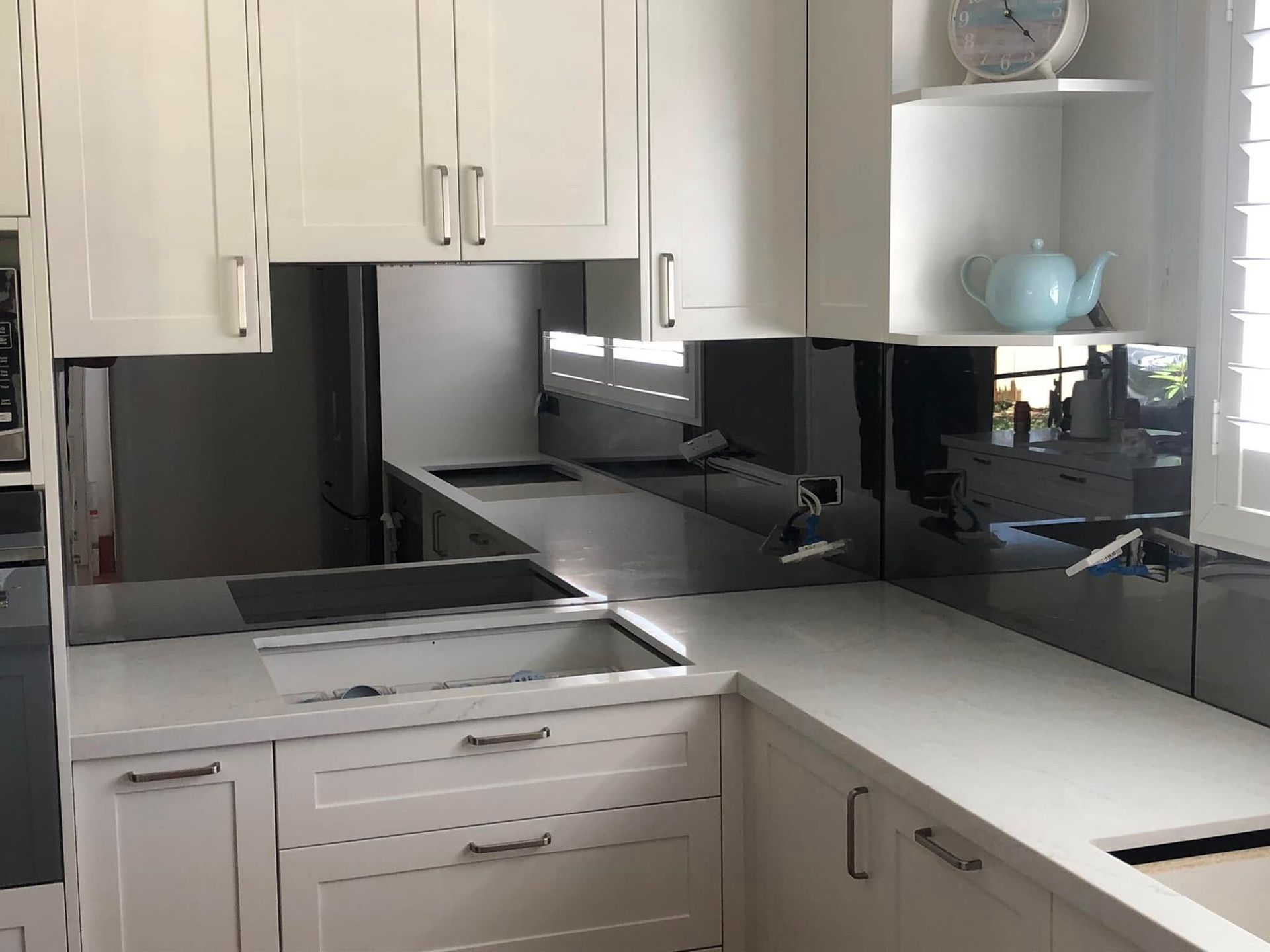 Modern kitchen with white cabinets, countertops, and dark-colored mirror backsplash reflecting the interior — Long Jetty Glass in The Entrance, NSW
