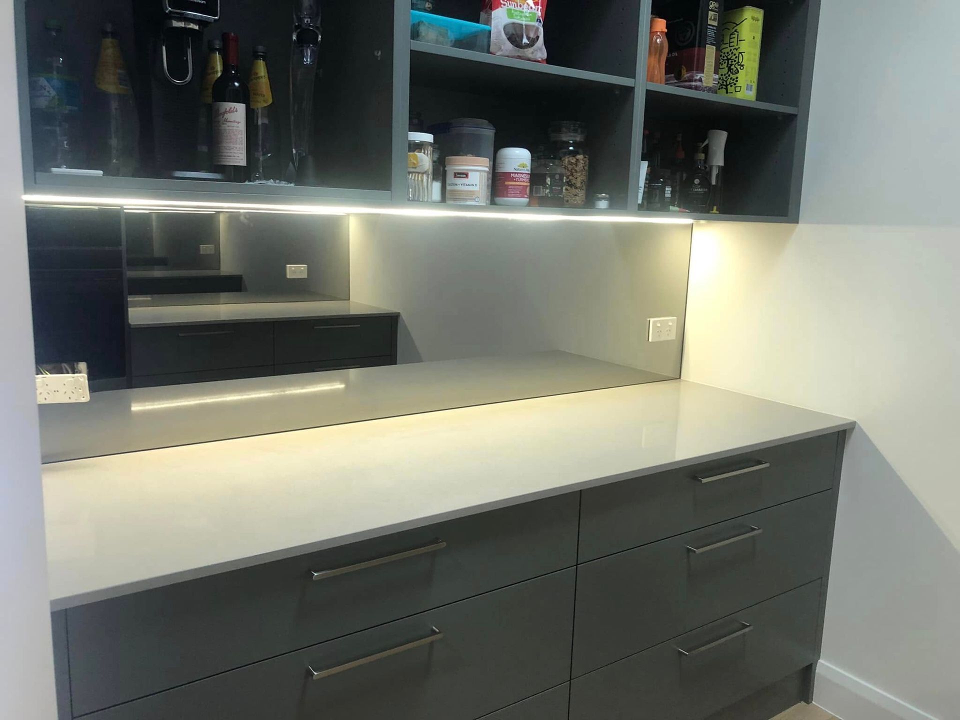 Grey kitchen cabinets with a light countertop and open shelving, backlit by LED lights — Long Jetty Glass in The Entrance, NSW