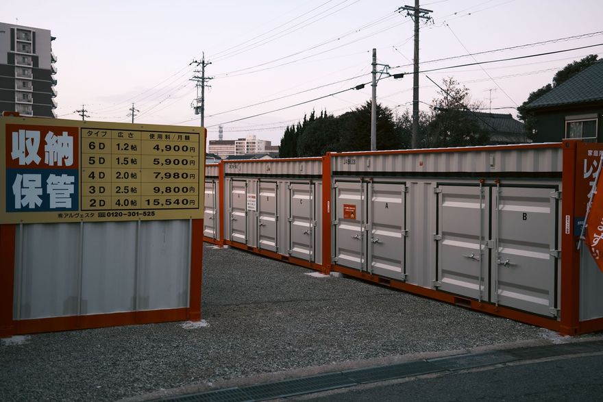 Rows of white storage containers behind orange fencing, with a Japanese sign at the entrance.