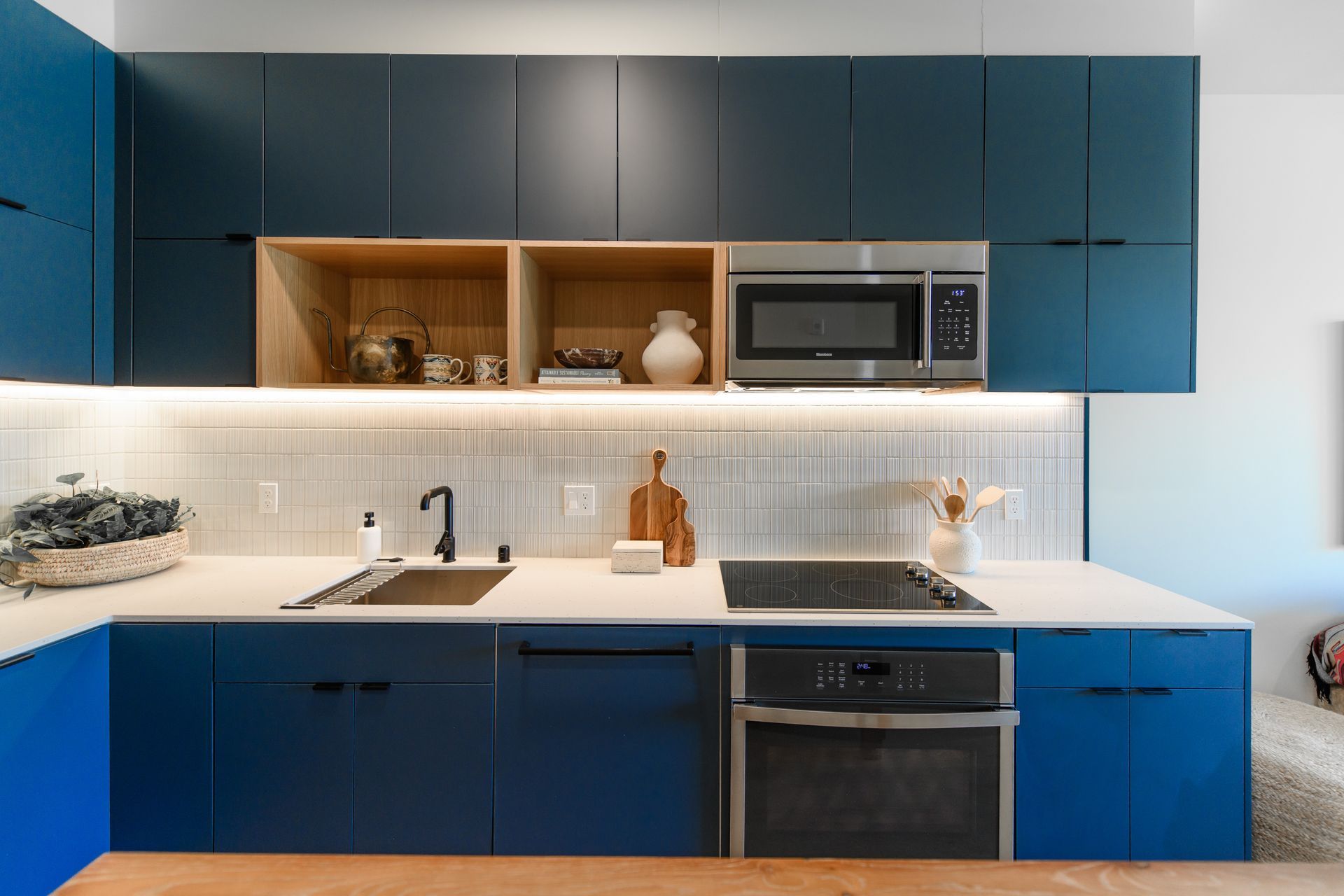 Blue kitchen with white countertops, wooden shelves, and stainless steel appliances.