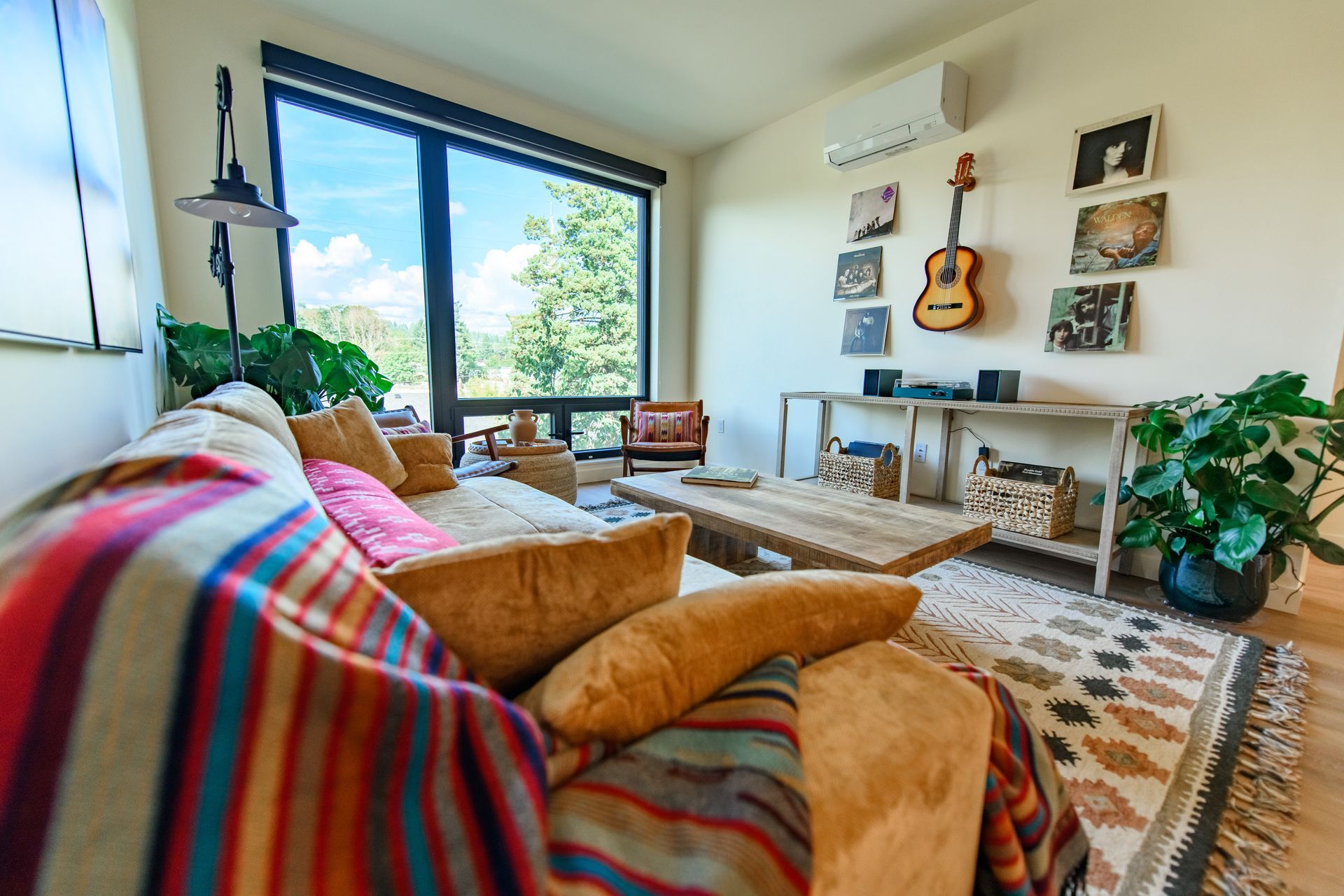 Cozy living room with large window, plants, record player, guitar, and patterned rug.
