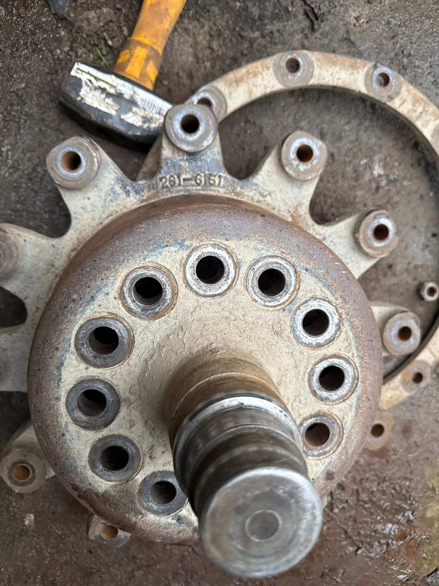 Close-up of a rusty metal hub with multiple holes, a ring, and a yellow hammer.