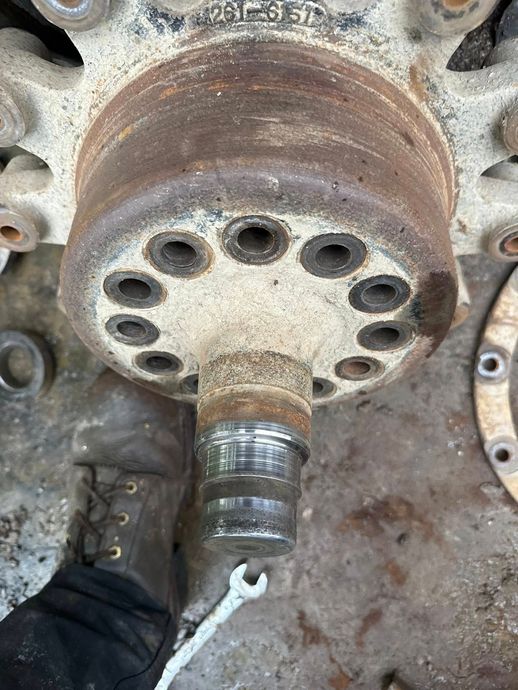 Close-up of a rusty wheel hub and axle. A person's boot and a wrench are at the bottom.