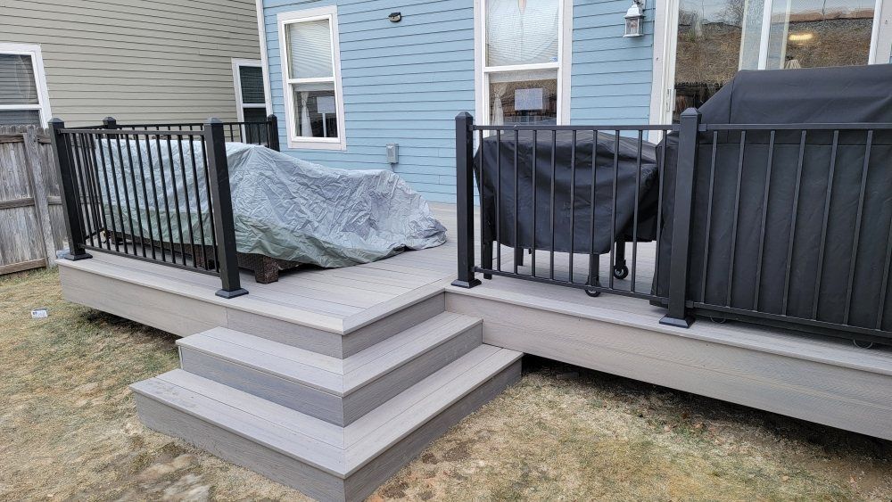 A light gray composite deck with black metal railings and a three-step staircase leading down to a lawn.