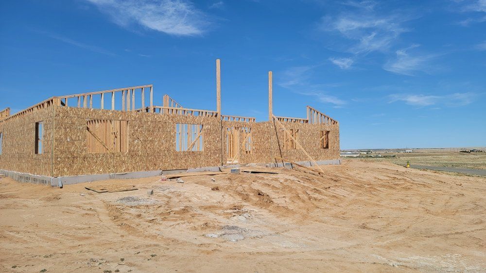 A wooden house frame under construction in a desert landscape under a clear blue sky.