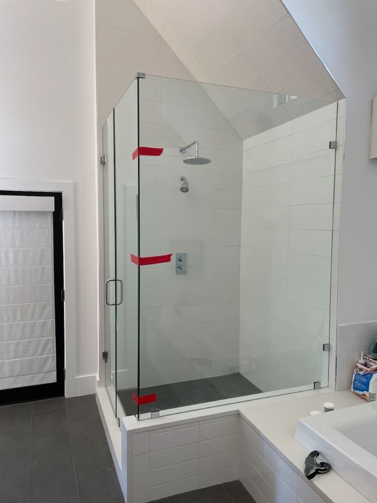 A glass shower enclosure with red tape on the hinges, positioned in a modern bathroom next to a white vanity.