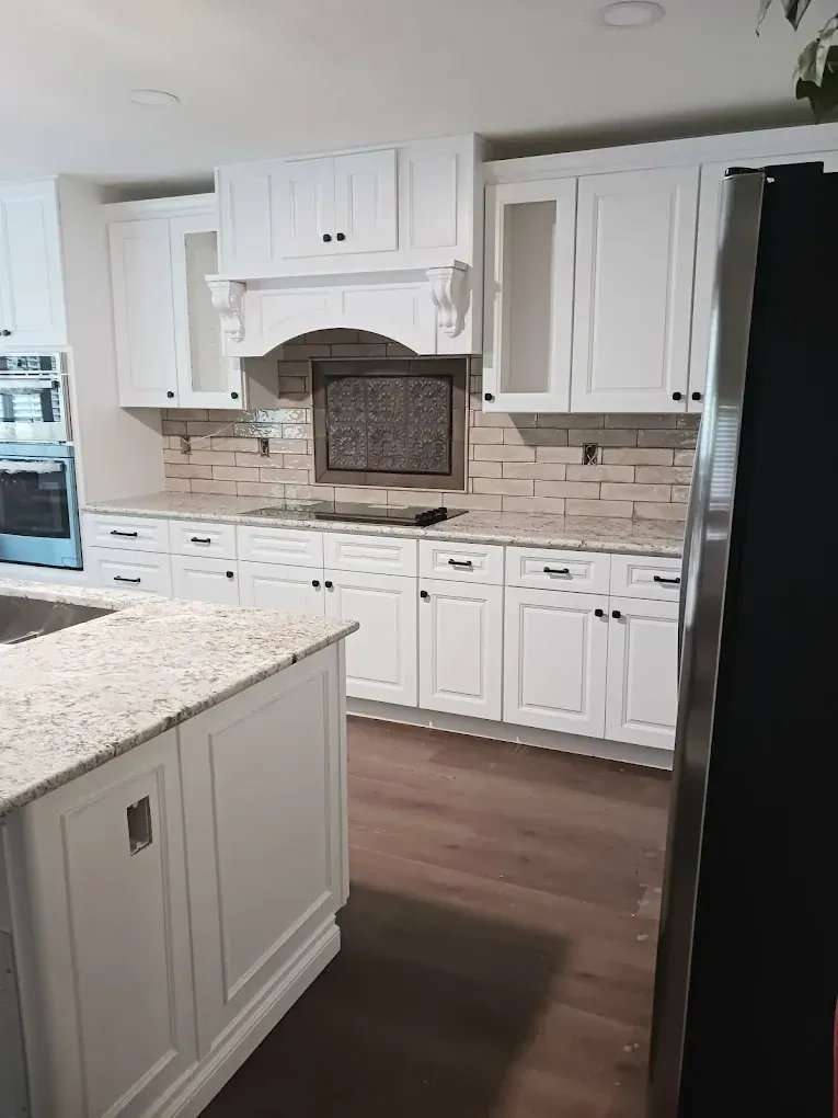 Modern kitchen featuring white cabinets, granite countertops, a brick backsplash, and hardwood floors.