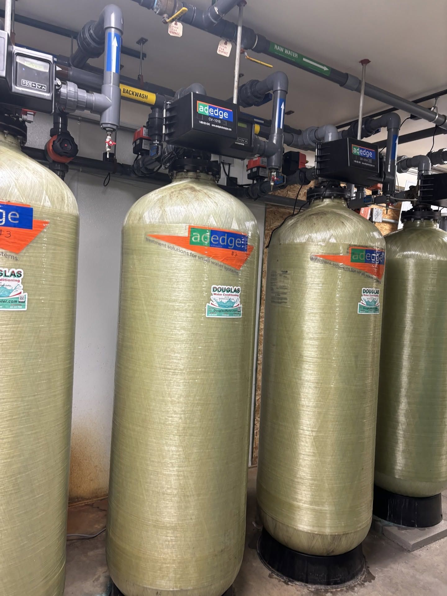Large industrial water filtration tanks with gauges and pipes in a mechanical room.