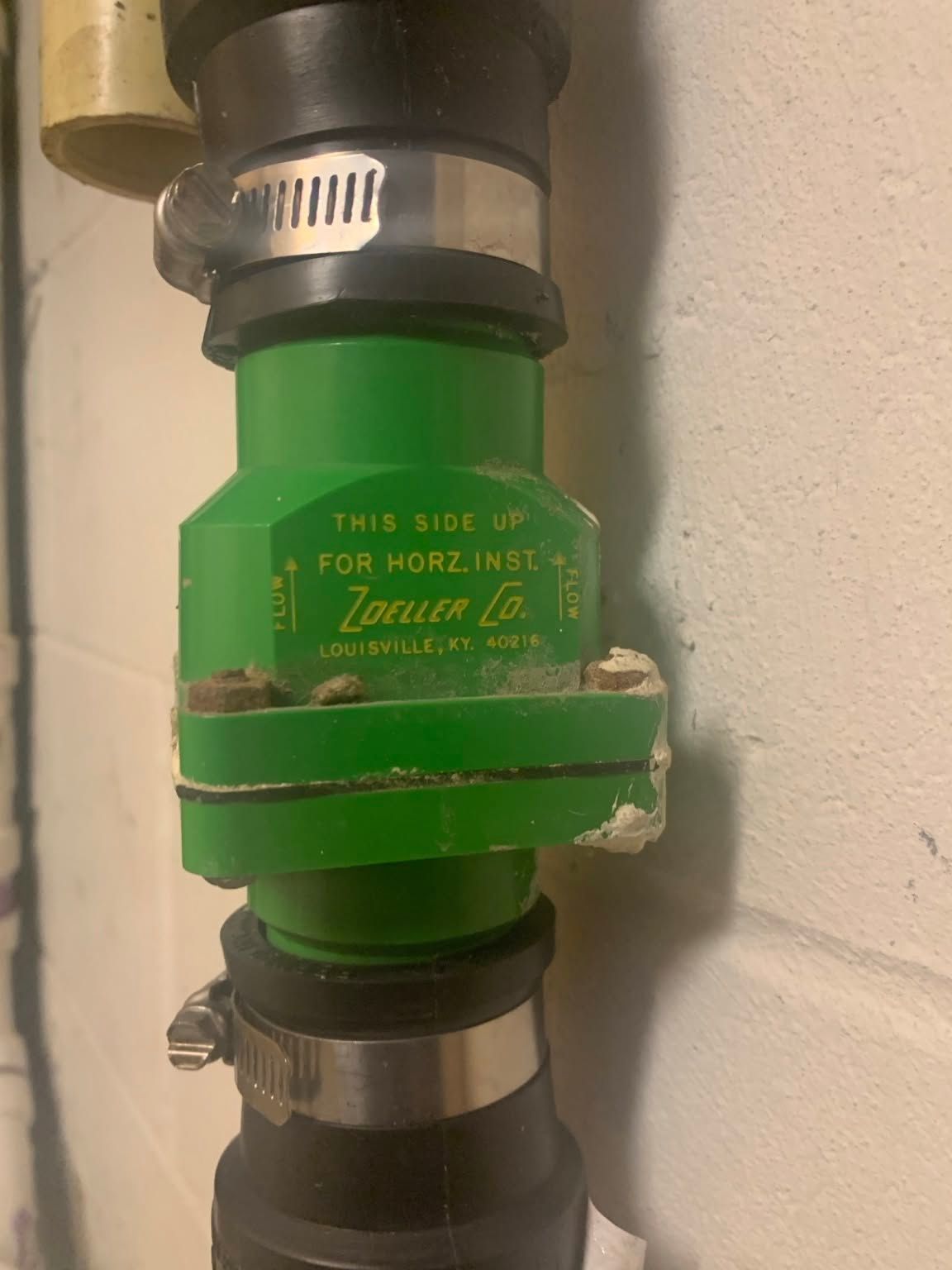 Green Zurn valve on vertical black pipes against a white wall.