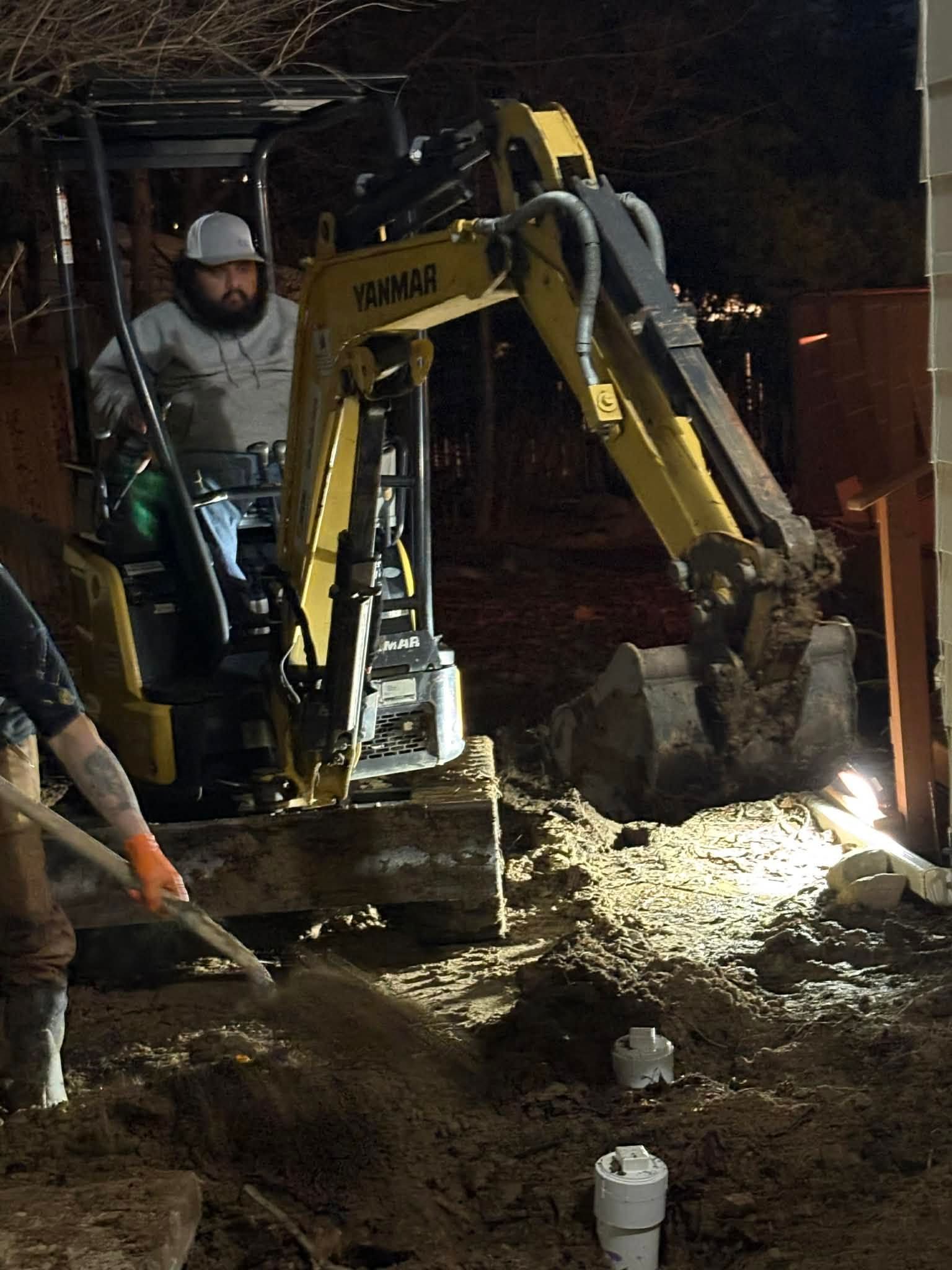 Worker operating a yellow excavator at night, digging in a muddy construction site with sparks nearby