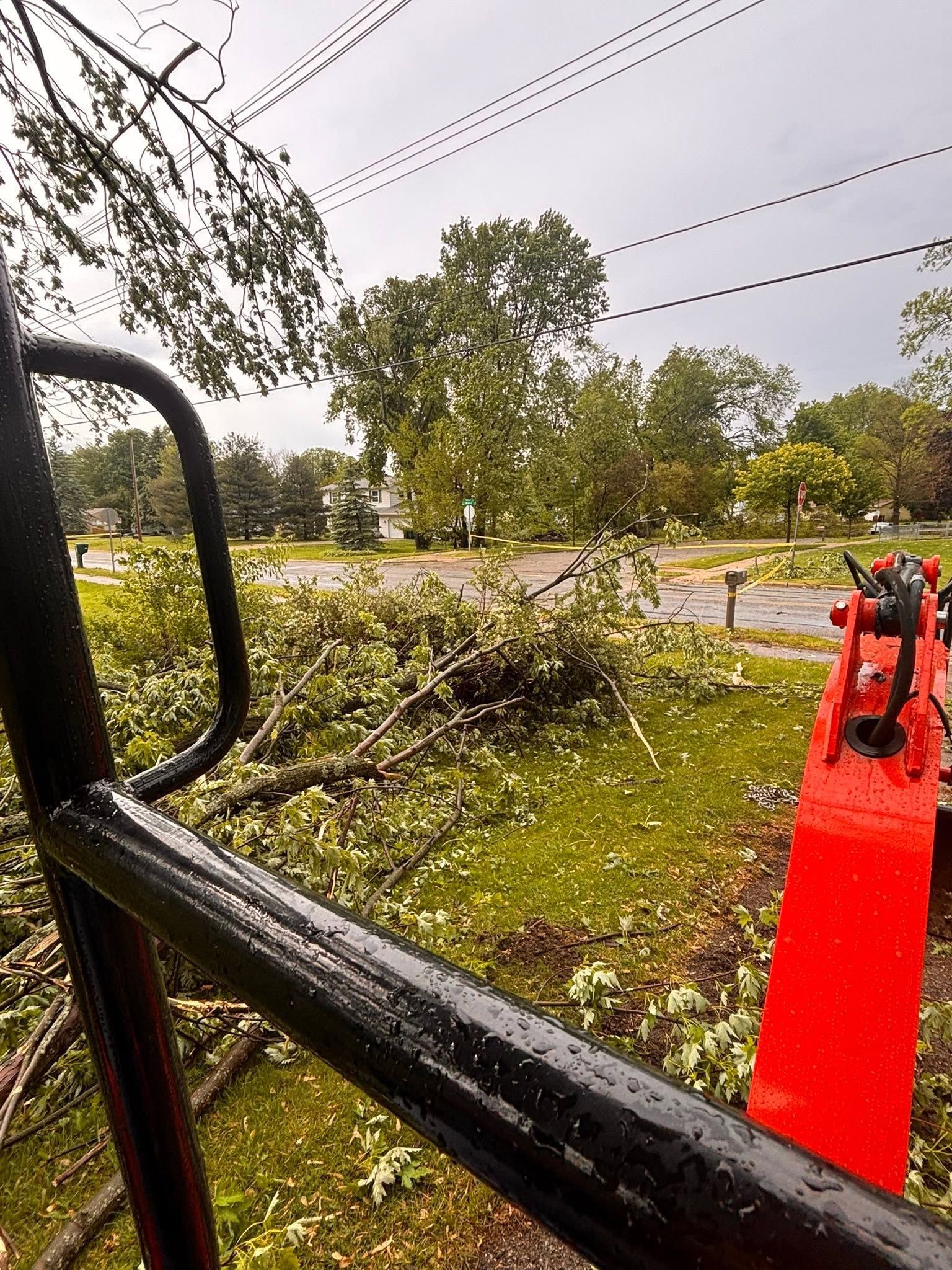 View from construction machinery over a road with fallen branches and a red boom arm in the foreground