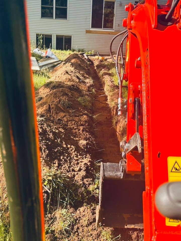 Trench being dug beside a house by an orange excavator